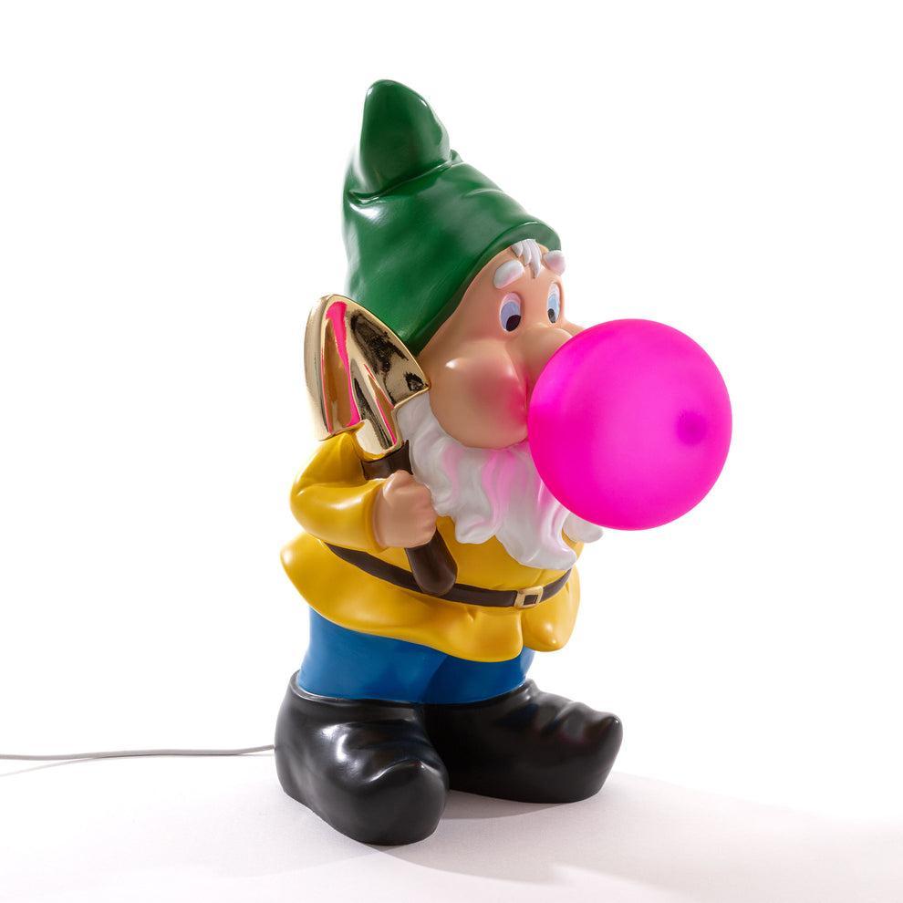 Lampada da tavolo Seletti gnomo in resina con cappello verde e bolla rosa accesa su fondo bianco