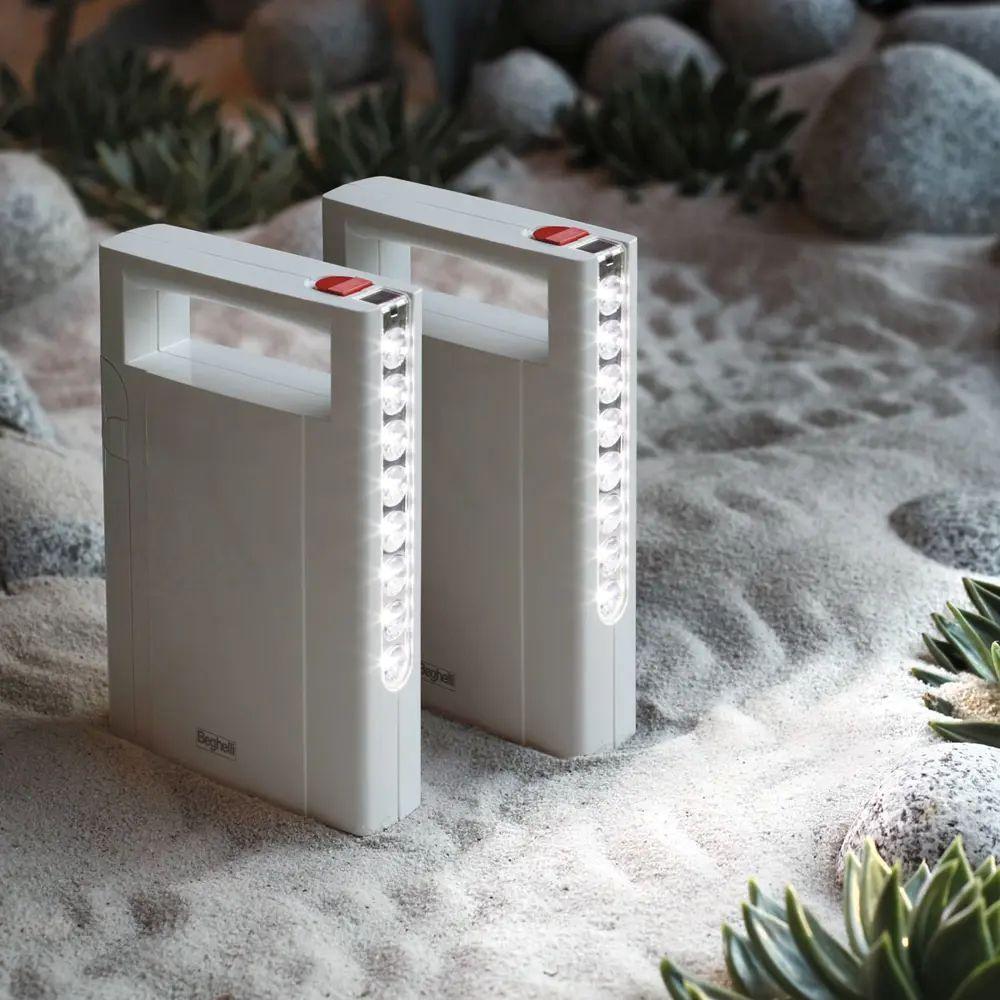 due lampade led beghelli portatili bianche accese su superficie sabbiosa per illuminazione di emergenza